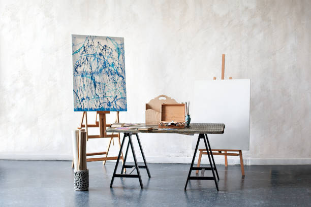 kreative künstler arbeitsplatz keine menschen hobbys. malstudio eines freischaffenden künstlers. easel, leinwand, pinsel, bleistifte, farben mit alben auf dem tisch. das interieur im atelier des künstlers, werkstatt - easel artists canvas paint paintings stock-fotos und bilder