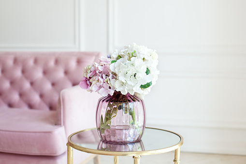 Bouquet of pastel hydrangeas in glass vase. Flowers in a vase at home. beautiful bouquet of hydrangeas is in a vase on a table near a pink sofa in a white living room. Home interior decor. Scandinavia