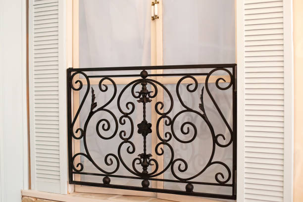 istock Old mediterranean window. French doors with wrought-iron balconies. A tiny balcony with wrought iron railings against a cream stone building with open shutters and closed French doors. Home interior 1182452947