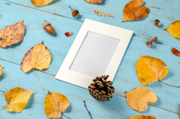 istock Autumn  composition  background.  Rusty yellow leaves ,  pinecone   and  acorn on blue background board with an empty photo frame for text   in the middle   . 1182456735