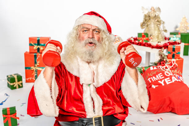 Santa Claus  making exercises.  The scene is located in a studio environment within prepared Christmas set with tree, presents, angels, lights, balls and other christmassy decoration. The footage is taken with Sony A7III camera.