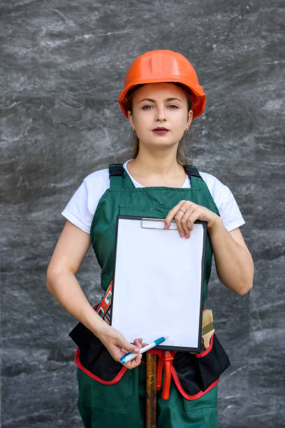 istock Woman in protective uniform and helmet posing with clipboard and tool belt 1182459069
