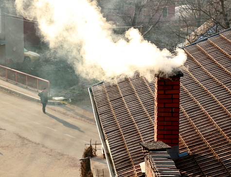 Smoke from the chimney on the roof of the house.