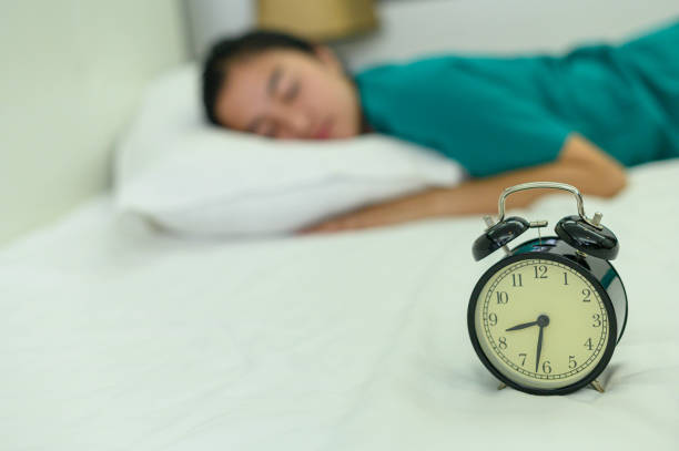 istock Sleeping girl on a white bed beside an alarm clock. 1182461724