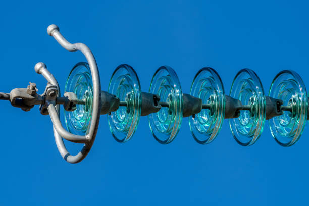 Close up of a transparent turquoise High voltage insulator or isolator in sunlight and clear blue sky