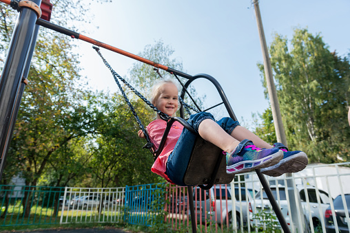 Happy elementary age girl smiles as she swings on a swing. The little girl has disabled arms and hands.