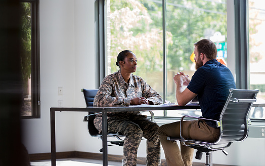 Attentive mid adult African American soldier attentively listens as a male therapist gives her advice.