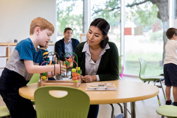 istock Female teacher sits to help young boy with bead puzzle 1182464398