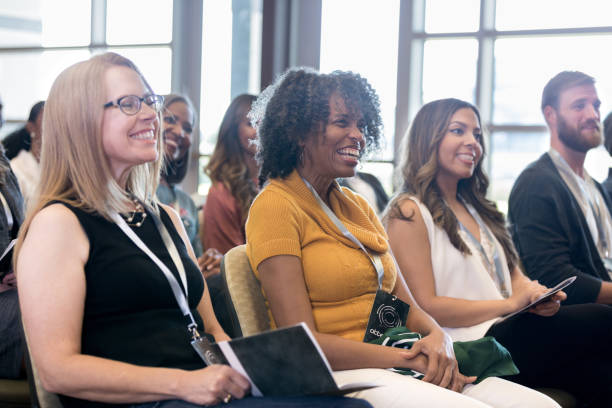 Attentive people smile during conference Diverse men and women attending a conference in a convention center. summit meeting photos stock pictures, royalty-free photos & images