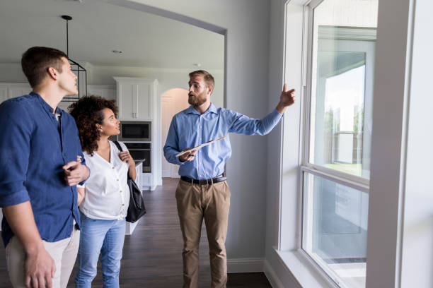 Male real estate agent shows new home Confident male Real Estate Agent shows potential homeowners a view from the living room windows in the home. inspector stock pictures, royalty-free photos & images