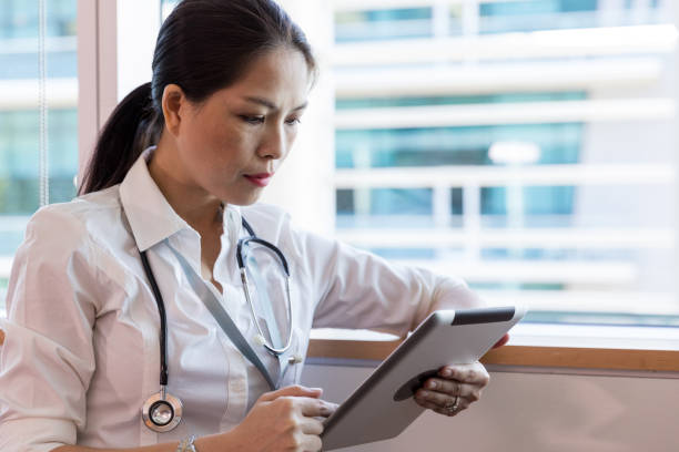 Mid adult doctor uses digital tablet to access patient records The mid adult female doctor uses a digital tablet to access patient records for the people she will see that day, hospital card stock pictures, royalty-free photos & images