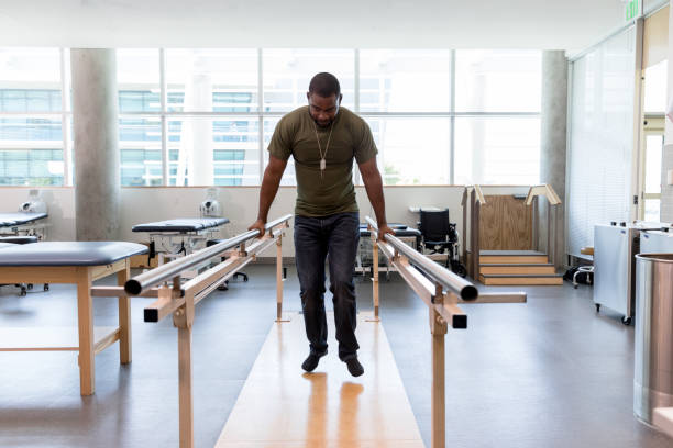 Soldier learns to walk in rehab clinic Mid adult military soldier uses parallel bars in a rehab center. black military man stock pictures, royalty-free photos & images