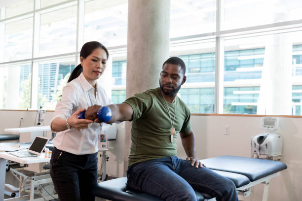 Injured soldier in physical therapy Serious army soldier with injury uses a hand weight during a physical therapy session. A female physical therapist is helping him with an exercise. black military man stock pictures, royalty-free photos & images