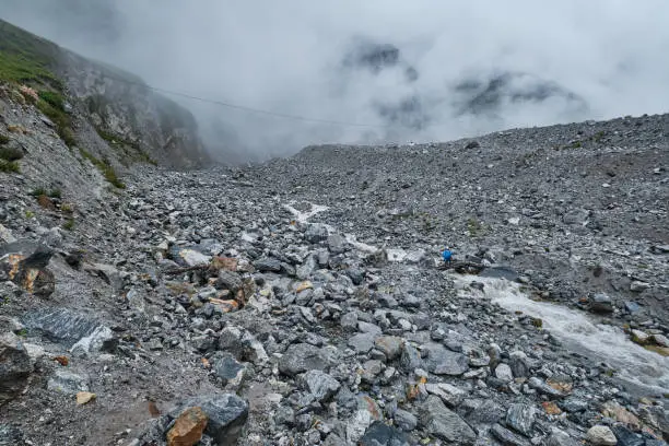 A small stream flowing across a rocky area formed from a landslide in Langtang Valley. A person can be seen crossing the fast flowing stream.