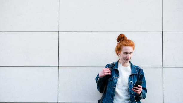 istock Young woman checks smart phone while standing by wall 1182465021