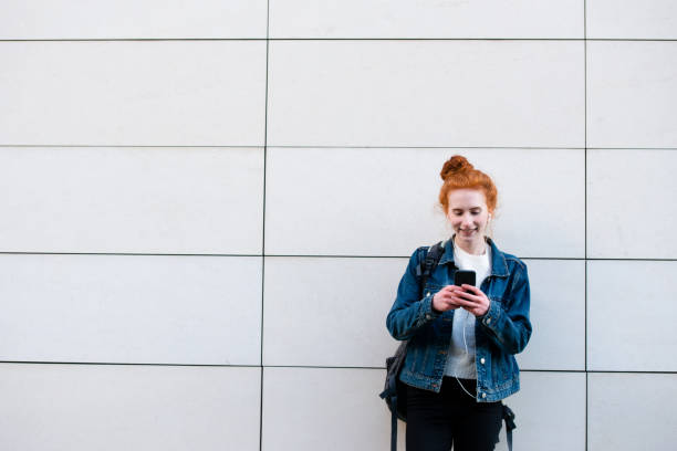 istock Student standing outside by wall smiles checking phone 1182465032