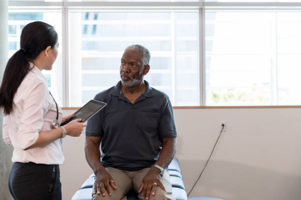 therapist uses digital tablet to diagnose mature patient's problem - outpatient imagens e fotografias de stock