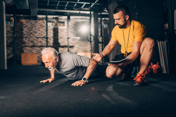 istock Active, sporty elderly man doing push-ups with his personal fitness trainer instructing him before an exercise session in a training gym 1182466290
