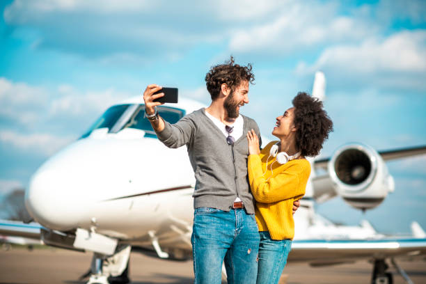 istock Rich young couple looking at each other while taking a selfie on a mobile phone in front of a private jet parked on an airport tarmac 1182466546