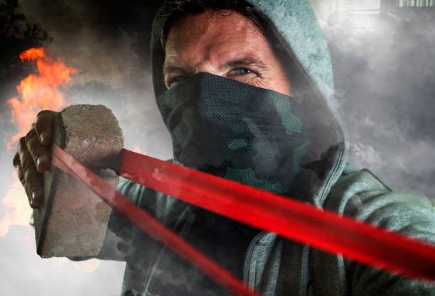 young man as ultra and radical anarchist rioter . furious antifa protester in face mask throwing brick hostile on street on demonstration in violet riot and chaos stock photo