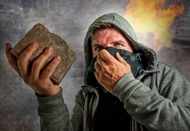 young man as ultra and radical anarchist rioter . furious antifa protester in face mask throwing brick hostile on street on demonstration in violet riot and chaos - throwing people stone tossing imagens e fotografias de stock