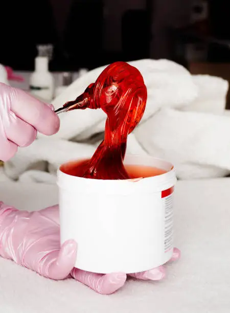 Photo of Beautician takes red transparent shugaring paste from a white can