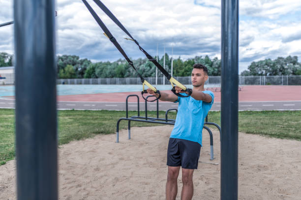 istock man athlete training with loops, straps for push-ups pull-ups, summer day city. Active youth lifestyle, fitness workout street. Free space strength and motivation. Strong man trainer. 1182470363