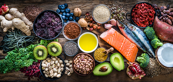 Top view of healthy, antioxidant group of food shot on rustic wooden table. The panoramic composition includes food rich in antioxidants considered as a super-food like avocado, kale, blueberries, chia seeds, coconut, broccoli, different nuts, salmon, sardines, pollen, quinoa, hemp seeds, seaweed, cocoa, olive oil, goji berries, flax seeds, kiwi fruit, pomegranate and ginger. XXXL 42Mp studio photo taken with SONY A7rII and Zeiss Batis 40mm F2.0 CF