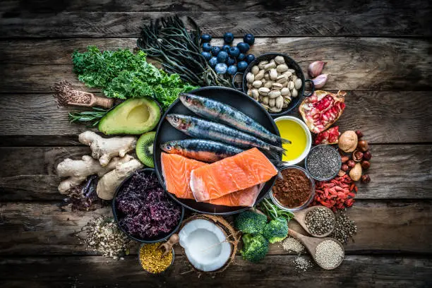 Top view of healthy, antioxidant group of food placed at the center of a rustic wooden table. The composition includes food rich in antioxidants considered as a super-food like avocado, kale, blueberries, chia seeds, coconut, broccoli, different nuts, salmon, sardines, pollen, quinoa, hemp seeds, seaweed, cocoa, olive oil, goji berries, flax seeds, kiwi fruit, pomegranate and ginger. XXXL 42Mp studio photo taken with SONY A7rII and Zeiss Batis 40mm F2.0 CF