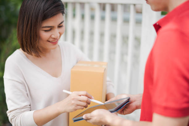 笑顔と落ち込む自宅の屋外で郵便配達員から小包段ボール箱を受け取るタブレット上の若いアジアの女性デジタルサイン技術、配達人は顧客に商品を出荷を表明 - 4810 ストックフォトと画像