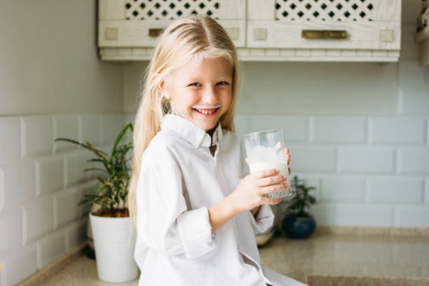 happy blonde long hair little girl drinking milk in kitchen, healthy lifestyle - milk child drinking little girls imagens e fotografias de stock