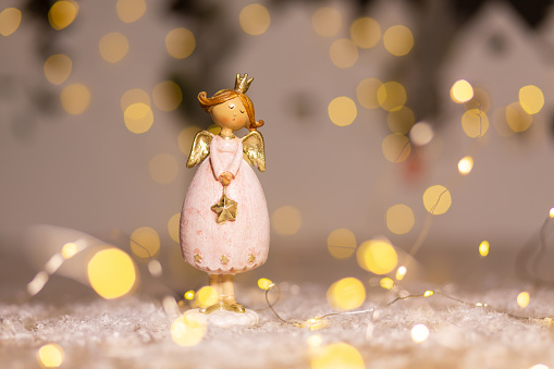 Decorative Christmas-themed figurines. Statuette of a Christmas angel. Christmas tree decoration. Festive decor, warm bokeh lights