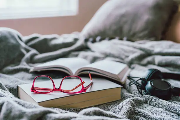 Shot of a book, glasses and headphones on a bed at home