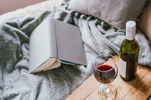 Shot of a glass of red wine and a book on the bed at home