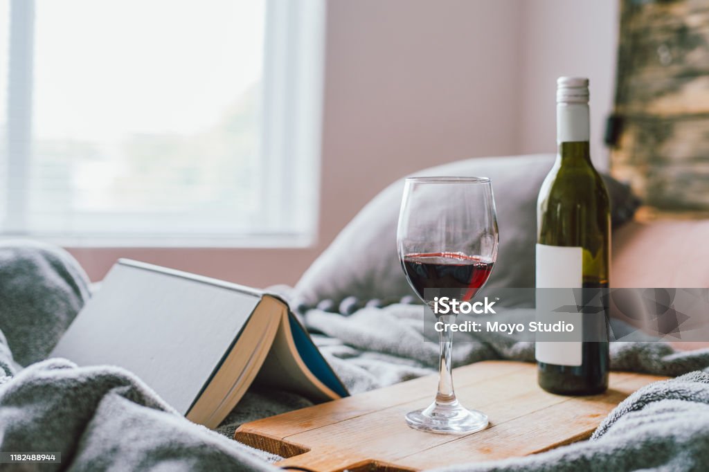 Just one more chapter... Shot of a glass of red wine and a book on the bed at home Wine Stock Photo
