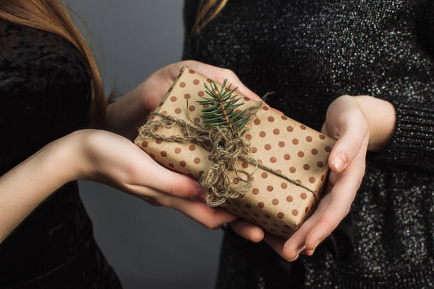 una chica le da a un amigo un regalo de navidad hecho con sus propias manos. el concepto de navidad y el nuevo año. chicas con vestidos negros brillantes intercambian regalos - holiday paper spotted close up fotografías e imágenes de stock