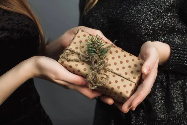 A girl gives a friend a Christmas gift made with her own hands. The concept of Christmas and the new year. Girls in shiny black dresses exchange gifts.