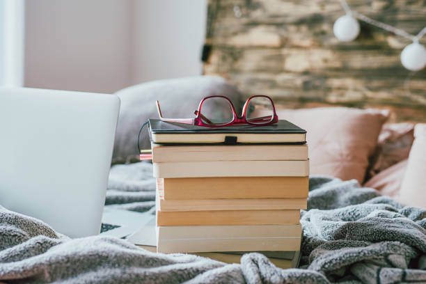 The mind can never get enough books Shot of a pile of books with glasses and a laptop on the bed at home naver stock pictures, royalty-free photos & images