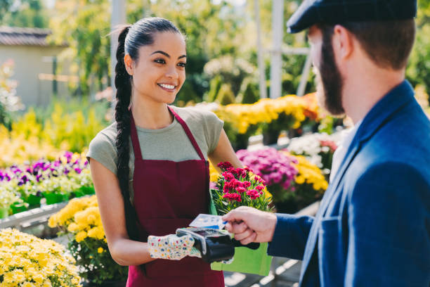 Customer at the flower market paying contactless with credit card Man buying potted flowers paying the florist with credit card flower market stock pictures, royalty-free photos & images