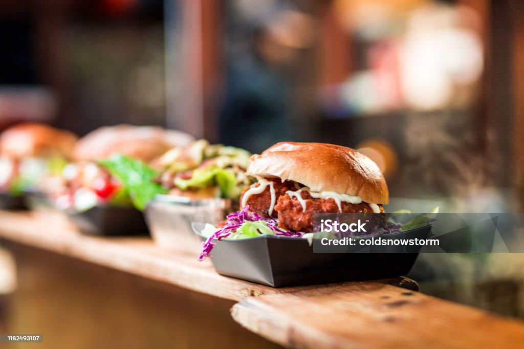 Fresh Crispy Pork Burgers in a row at Food Market Close up image depicting a burger loaded with crispy fried pork balls on display and for sale at an outdoors food market. The background of the market stall is totally defocused, leaving room for copy space. Food Stock Photo