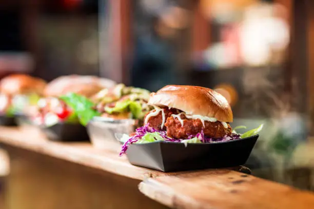 Close up image depicting a burger loaded with crispy fried pork balls on display and for sale at an outdoors food market. The background of the market stall is totally defocused, leaving room for copy space.