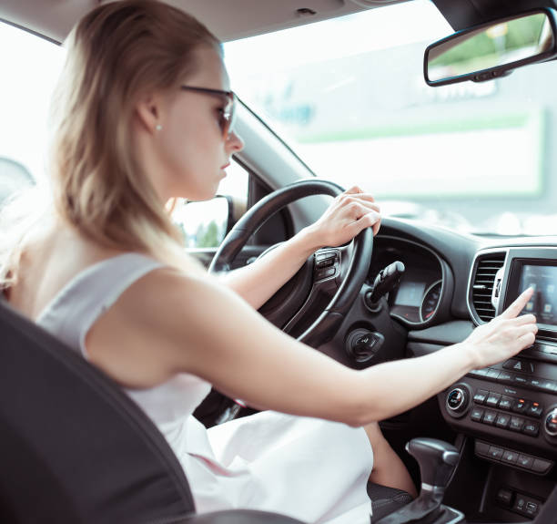 istock Girl driving car in cabin. Presses on touch screen, selects application. Activate and enable navigation. In summer in city in parking lot near shopping center. 1182502445