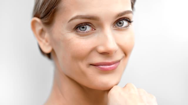 Beautiful female face with first wrinkles smiling looking at camera isolated at light background