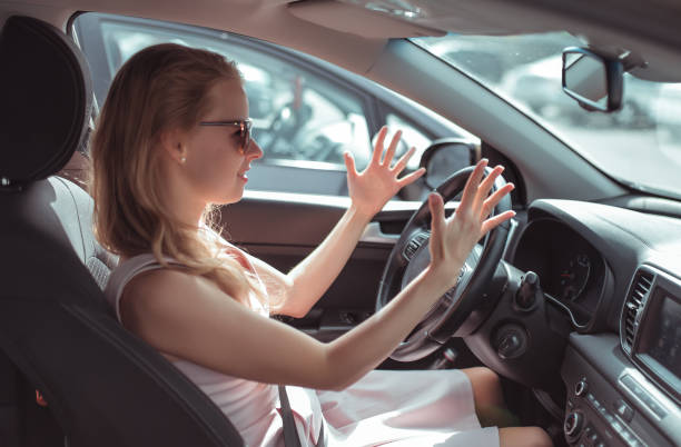 Girl driving car in cabin. Hand gesture accident signal conflict, emotions stress aggression discontent. Pink dress summer in parking lot mall. Misunderstanding scandal and accident on road. stock photo