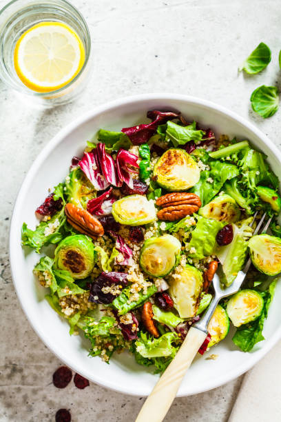 ensalada de coles de bruselas fritas con quinua, arándanos y nueces en tazón blanco, vista superior. concepto de comida vegana saludable. - col de bruselas fotografías e imágenes de stock