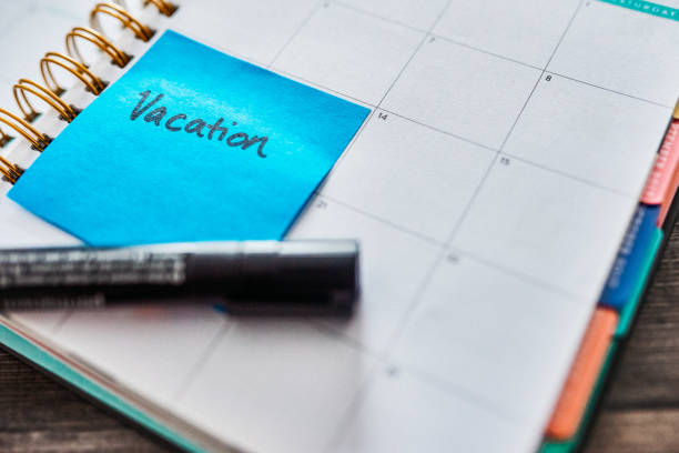 Shot of a notebook and a sticky note saying “vacation” stuck to it on a desk