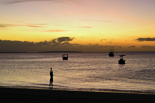 Girl silhouette and boats moored in Indian ocean at sunset, Kendwa, Zanzibar, Tanzania, Africa