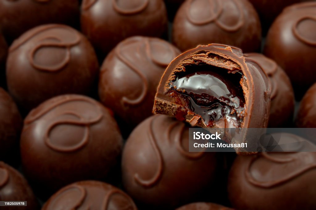 Sweet confectionery and candy indulgence concept theme with close up on a bitten cherry filled chocolate praline on top of many other delicious pralines with copy space Chocolate Stock Photo