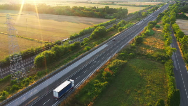 Aerial Drone Footage: Long Haul Semi Trucks Driving on the Busy Highway in the Rural Region of Italy. Agricultural Crop Fields and Hills in the Background