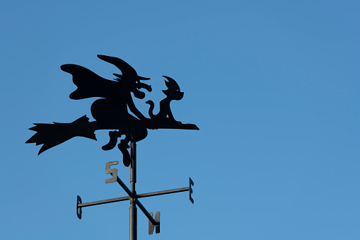 The weather vane witch with her cat is riding her broomstick north-east in sunny weather with clear blue skies.